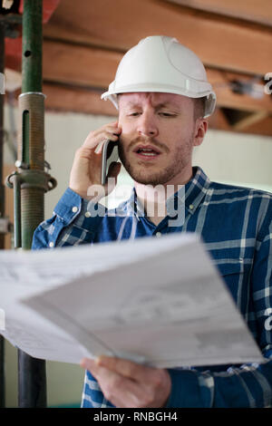 Architect Inside House Being Renovated Studying Plans Talking On Mobile Phone Stock Photo