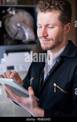 Male Heating Engineer Servicing Central Heating Boiler Using Digital Tablet Stock Photo