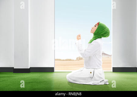 Pretty asian woman in veil sitting in praying position on the carpet rise the hands and looking up inside the room with open door and blue sky backgro Stock Photo