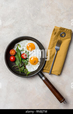 Pan and fried eggs for breakfast with herbs at beige background. Concept of breakfast dish. View from above. Stock Photo