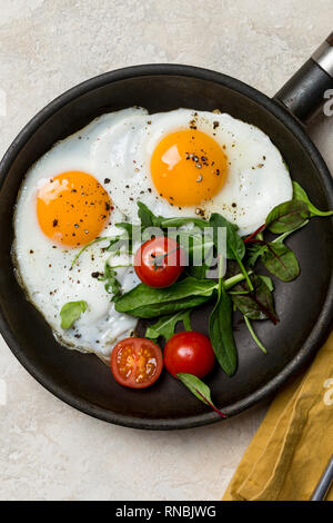 Close up picture. Two fried eggs with fresh salad on fried pan at white background, with orange napkin Stock Photo