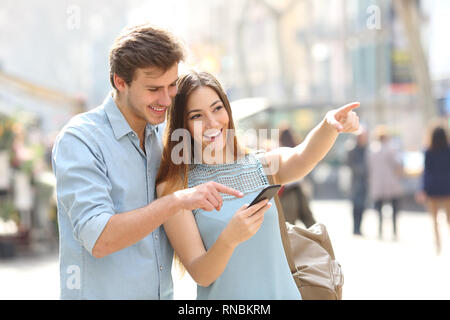 Happy friends or couple checking location on smart phone in the street Stock Photo