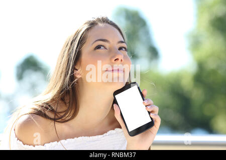 Pensive girl showing at camera blank smart phone screen mockup in a park Stock Photo