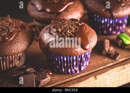 Chocolate muffins with ganache on a wooden serving tray. Closeup view of tasty chocolate cakes. Toned image. Stock Photo