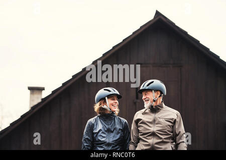 Active senior couple with bike helmets standing outdoors in front of a house. Stock Photo