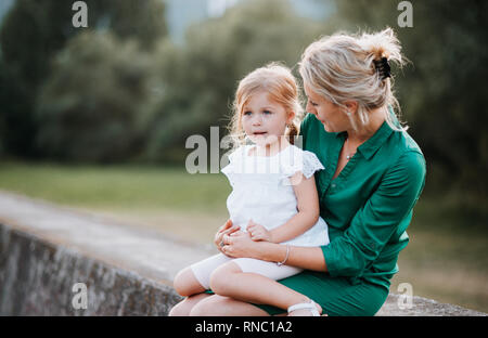 Young mother in nature with small daughter, sitting on a stone wall. Stock Photo