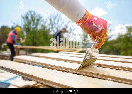 Painter holding a paintbrush over wooden surface, protecting wood for exterior influences and weathering. Carpentry, wood treatment, hard at work, hom Stock Photo