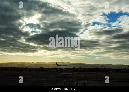 View of an aeroplane landing at Adelaide Airport against the backdrop of a morning sunrise and beautiful clouds. Stock Photo