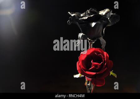 living and non-living. Hand holds graceful wrought-iron rose on a stand. In the background, a real yellow rose Stock Photo