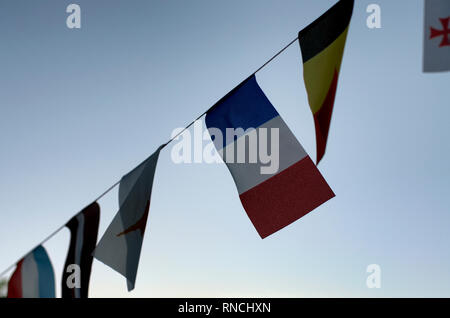 On the rope hangs the flag of France and a few flags on the background of the blue sky Stock Photo