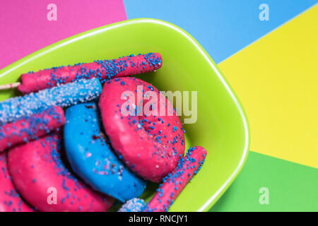 Blue and pink glazed donuts with sprinkles and candy sticks in bowl on the colorful background, close-up view with selective focus. Stock Photo