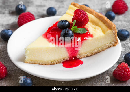 slice of cheesecake with fresh raspberries, blueberries, jam and mint on concrete background. close up. tasty breakfast Stock Photo