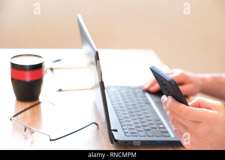 Smartphone in the hands of SMS mode. Coffee in glass. Glasses and notebook ready to go. Laptop on a light table. Ready for operation. Selective focus Stock Photo