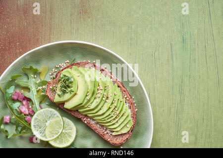 Avocado sandwich and green salad with ham cubes on brown-green textured background, top view with copy-space Stock Photo