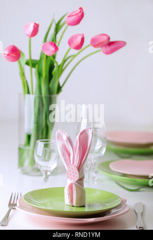 Happy easter. Decor and table setting of the Easter table is a vase with pink tulips and dishes of pink and green color. Selective focus. Stock Photo