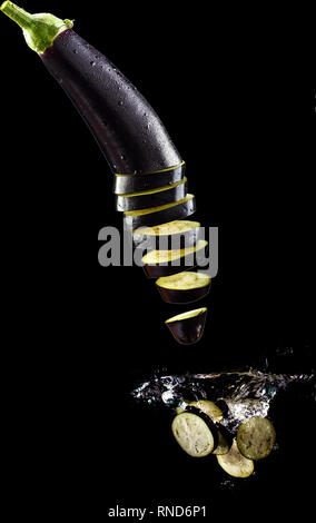 Tomato, two types of paprika and eggplant slices fall into water, on black background Stock Photo