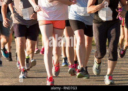 A pack of runners competing in a local five thousand meter race, both men and women together, on a sunny summer early evening Stock Photo
