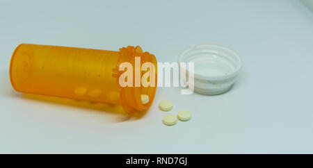 An almost empty prescription bottle is laying on the ground with pills spilling out. Stock Photo