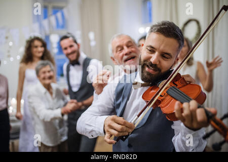 A mature man playing a violin on a wedding reception, bride and groom dancing. Stock Photo