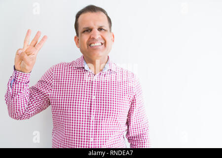 Middle age man wearing business shirt over white wall showing and pointing up with fingers number three while smiling confident and happy. Stock Photo