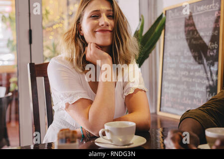 Happy young woman sitting at cafe with her friend. Relaxed female sitting at coffee shop with a male friend. Stock Photo