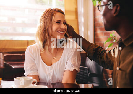 Interracial couple sitting at coffee shop. Smiling woman with her caring boyfriend at cafe. Stock Photo