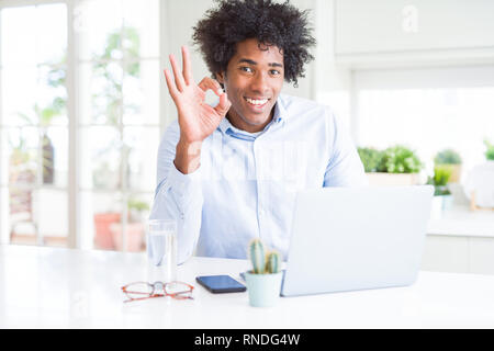 African American business man working using laptop doing ok sign with fingers, excellent symbol Stock Photo