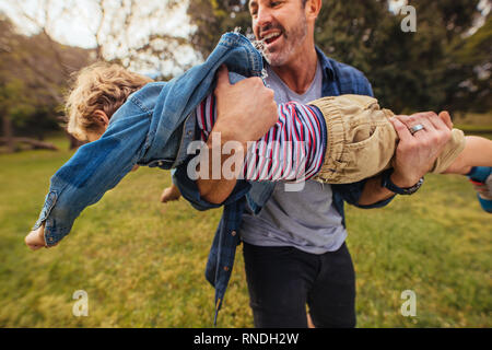 Man carrying little boy in hand and running in park. Father playing with son outdoors. Stock Photo