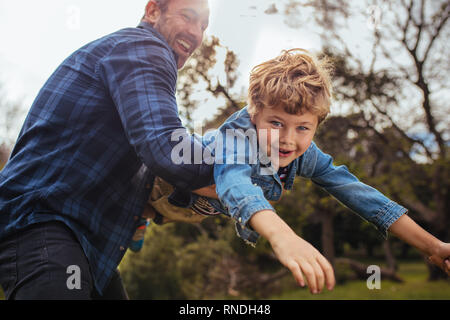 Little boy flying in arms of his dad. Small kid playing and having fun with his father at the park.