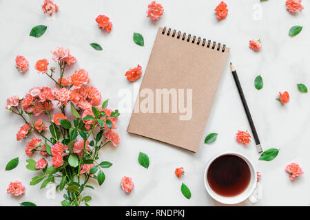 blank notepad with bouquet of rose flowers in Living Coral color and coffee cup in frame made of buds on white marble table. wedding background. Flat  Stock Photo