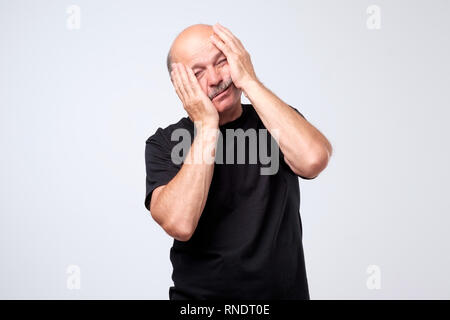 Studio shot of desperate upset senior man holding hands on face Stock Photo