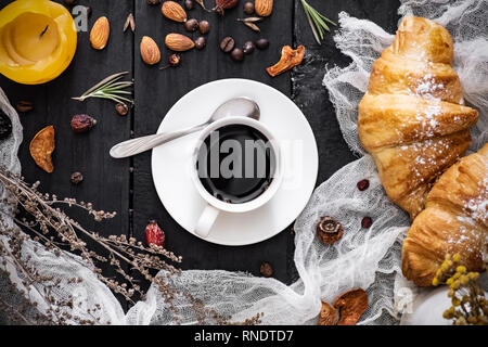 Cup of black coffee and croissants on black background, top view. Flat lay of espresso and cornetto rolls on dark rustic table