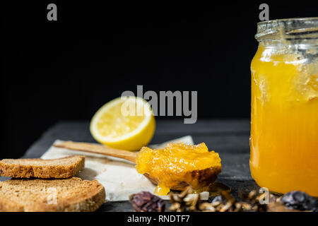 Spoonful of honey on dark rustic background. Crystallized home-made honey in jar, low-key shot Stock Photo