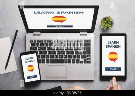 Learn Spanish concept on laptop, tablet and smartphone screen over gray table. All screen content is designed by me. Flat lay Stock Photo