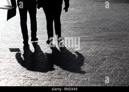 Silhouettes of two people walking down the street. Couple outdoors, people shadows on pavement, concept for for dramatic stories Stock Photo