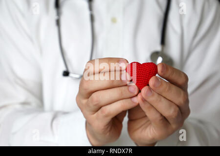 Cardiologist appointment, doctor with stethoscope holding red knitted heart in hands. Concept of cardiology, heart diseases, diagnosis, medical exam Stock Photo