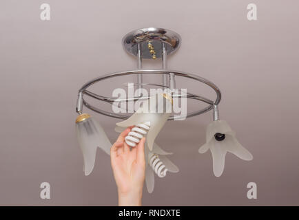Installing an energy-saving modern spiral light bulb in a chandelier suspended from the ceiling, energy saving, hand, close-up, equipment Stock Photo