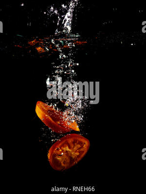 Tomato, two types of paprika and eggplant slices fall into water, on black background Stock Photo