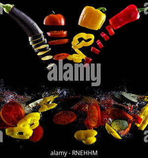 Tomato, two types of paprika and eggplant slices fall into water, on black background Stock Photo