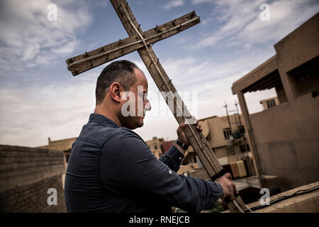 The former Christian war hero Husam S Tosh erects a wooden cross on the roof of a house in Karakosch near Mossul, which was used by the IS as a base camp and is used today as Christian party headquarters. The Christian population was expelled by the IS, but many return to their homes in the surrounding Christian villages. Some churches could be rebuilt, so that church services can take place there again. Nevertheless, the Christians are now threatened by the Shiite conquerors of the province Ninawa and the capital Mossul and more and more repressed, so that the Christians do not have good pers Stock Photo