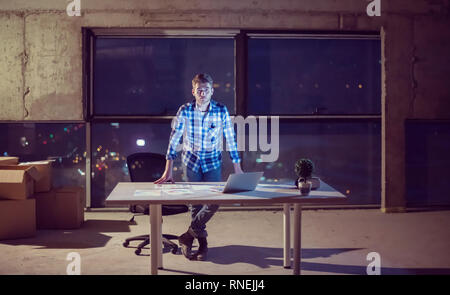 portrait of young male engineer on construction site checking documents and business workflow using laptop computer in new startup office at night Stock Photo
