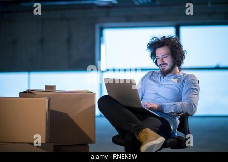 young male architect on construction site checking documents and business workflow using laptop computer with cardboard boxes around him in new startu Stock Photo