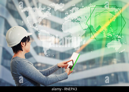 Confident young woman engineer wearing protective helmet holding a pc tablet computer using gadget to display a world map hologram choosing destinatio Stock Photo
