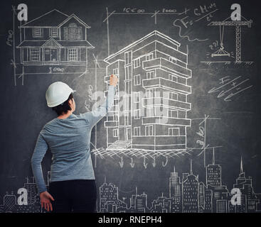 Rear view of creative young woman civil construction engineer or architect wearing protective helmet confident drawing different project sketches on b Stock Photo