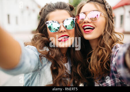 Gorgeous brunette girlfriends with hairstyle, mirrored sunglasses and red lips making selfie with duck face. Stock Photo