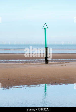 A green beach safety marker with a triangle on the top and an offshore windfarm in the distance off Rhyl beach, Denbighshire, North Wales Stock Photo
