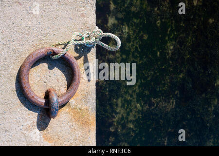 An old and rusty boat mooring ring set into the harbour concrete Stock Photo