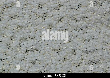A swatch of white woolen knit from a cardigan with small traces of gold fleck thread sewn into the garment. Stock Photo
