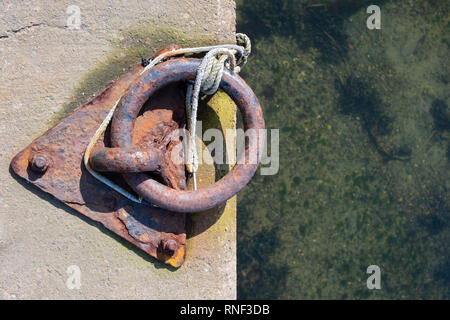 An old and rusty boat mooring ring set into the harbour concrete Stock Photo