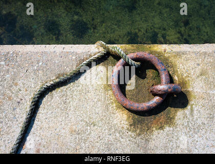 An old and rusty boat mooring ring set into the harbour concrete Stock Photo